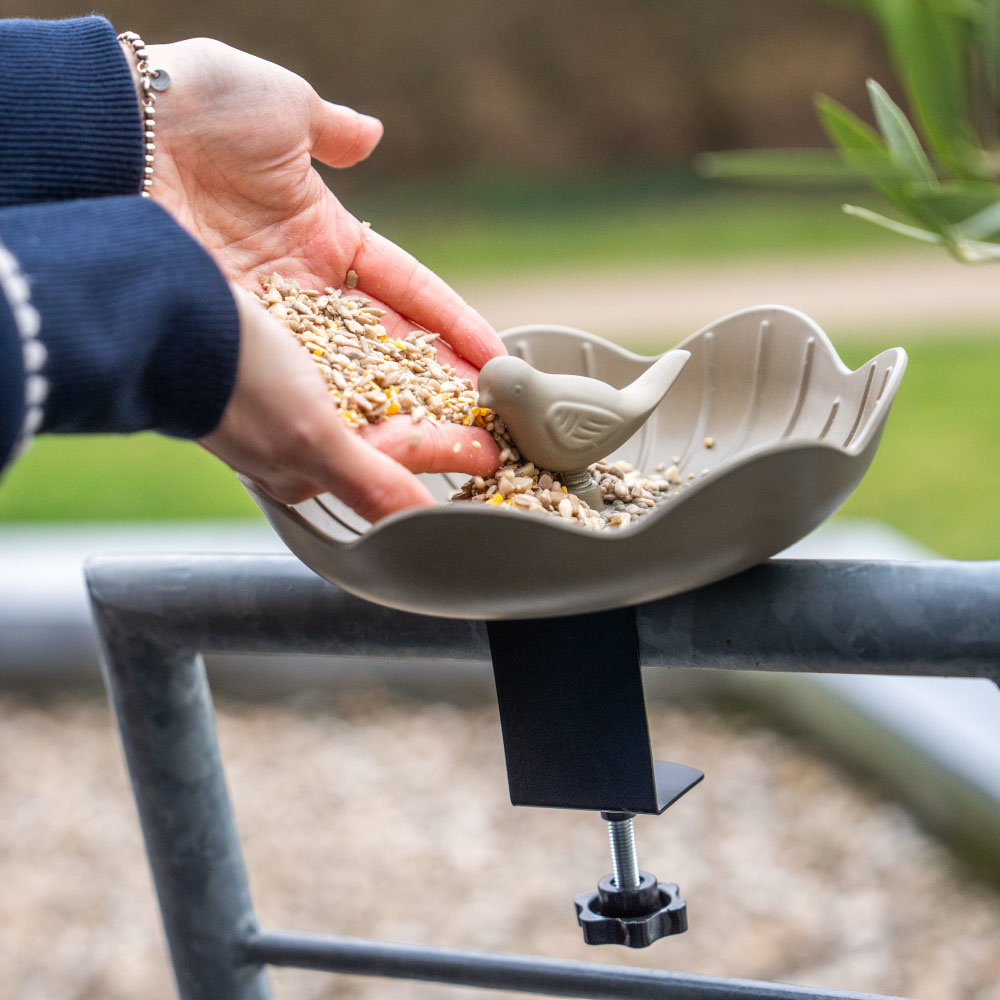 Een persoon vult een vogelvoederbak met vogel voer